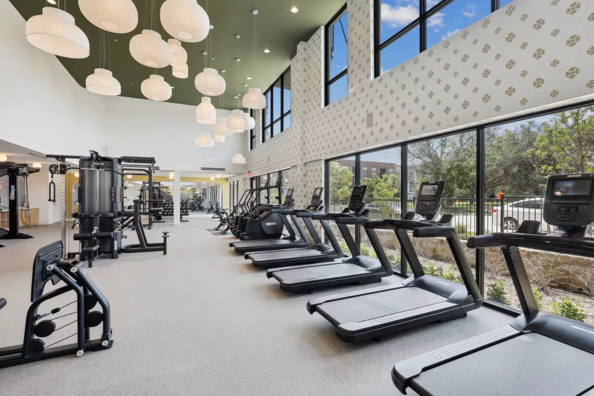 Modern gym with rows of treadmills and other equipment, under stylish hanging lights.