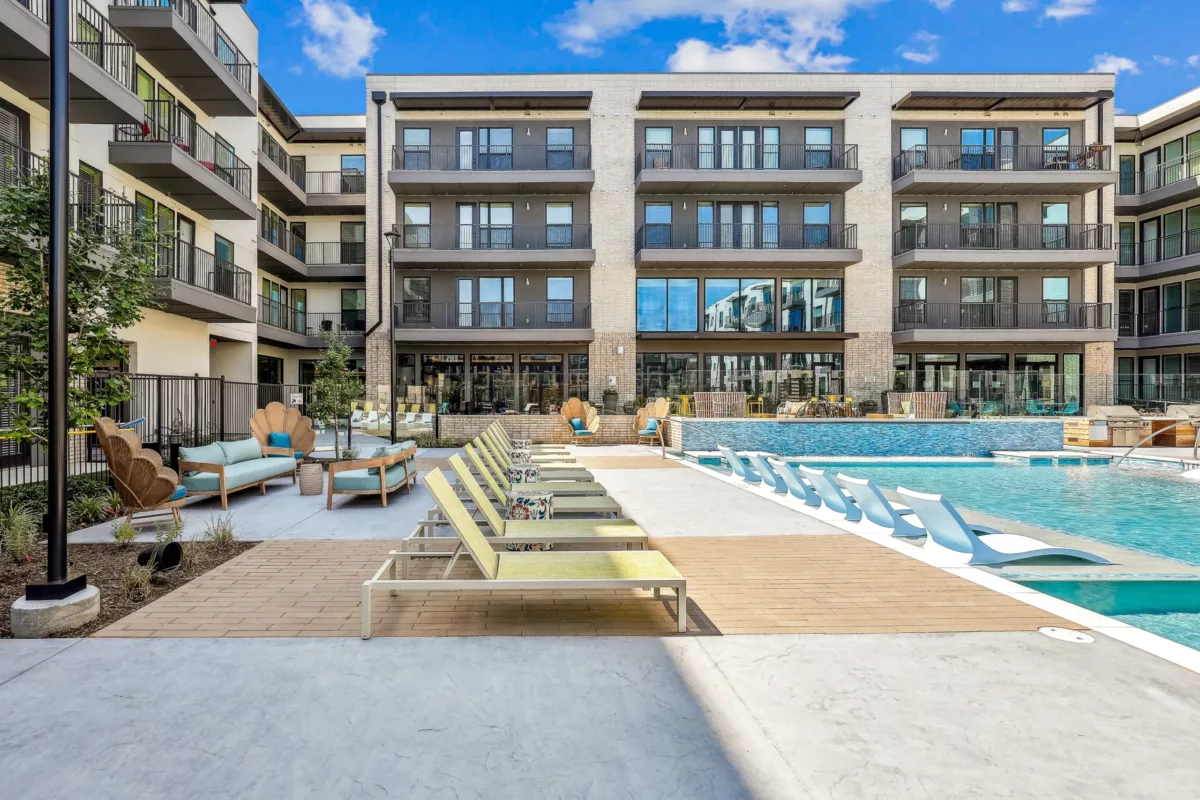 Modern outdoor pool area surrounded by multistory apartments, featuring lounge chairs and cozy seating.