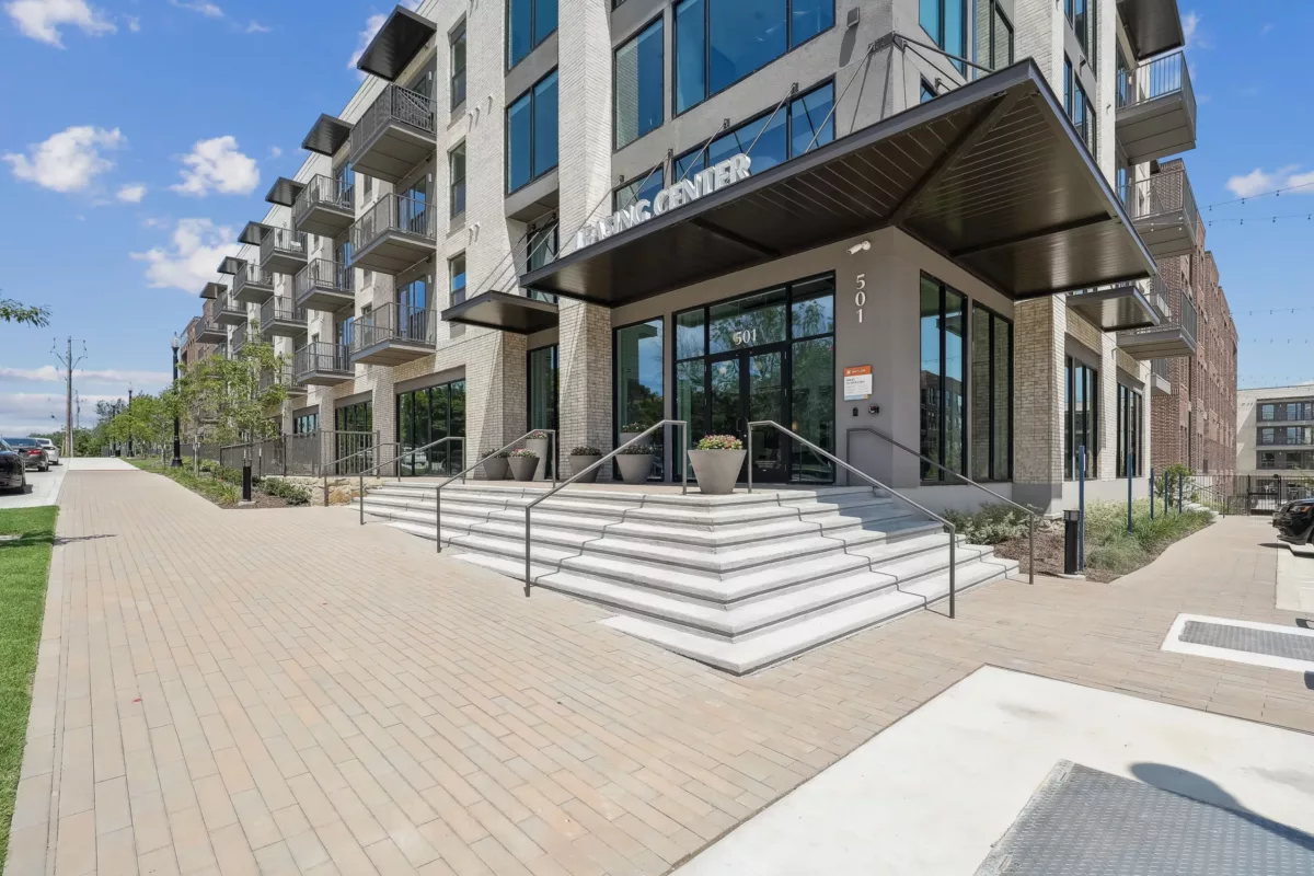 Modern residential building entrance with large steps and a canopy, leading to a lobby.