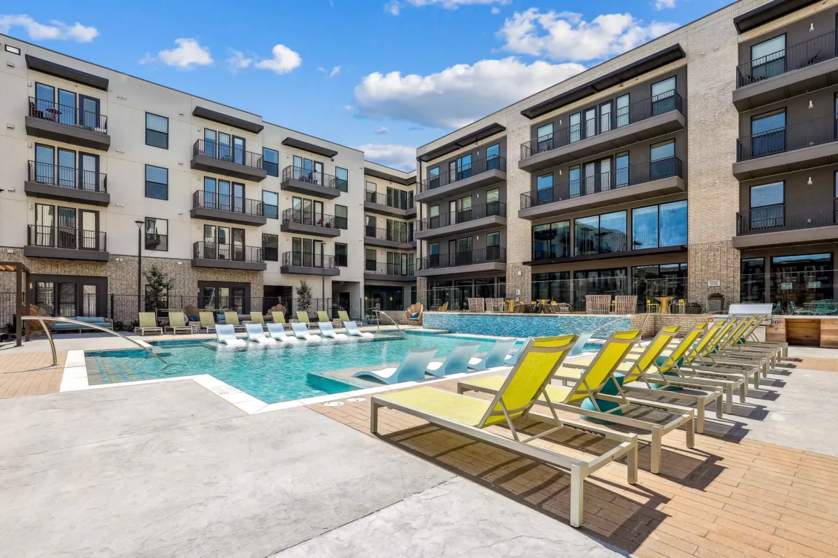 Resort-style outdoor pool area with sun loungers and contemporary apartment buildings around.