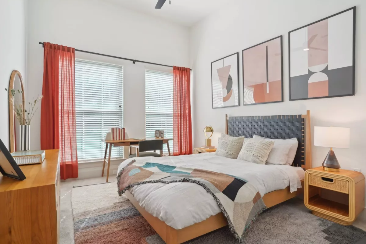 Bedroom with large windows with pink curtains, bed with fabric headboard, and artwork on the wall.